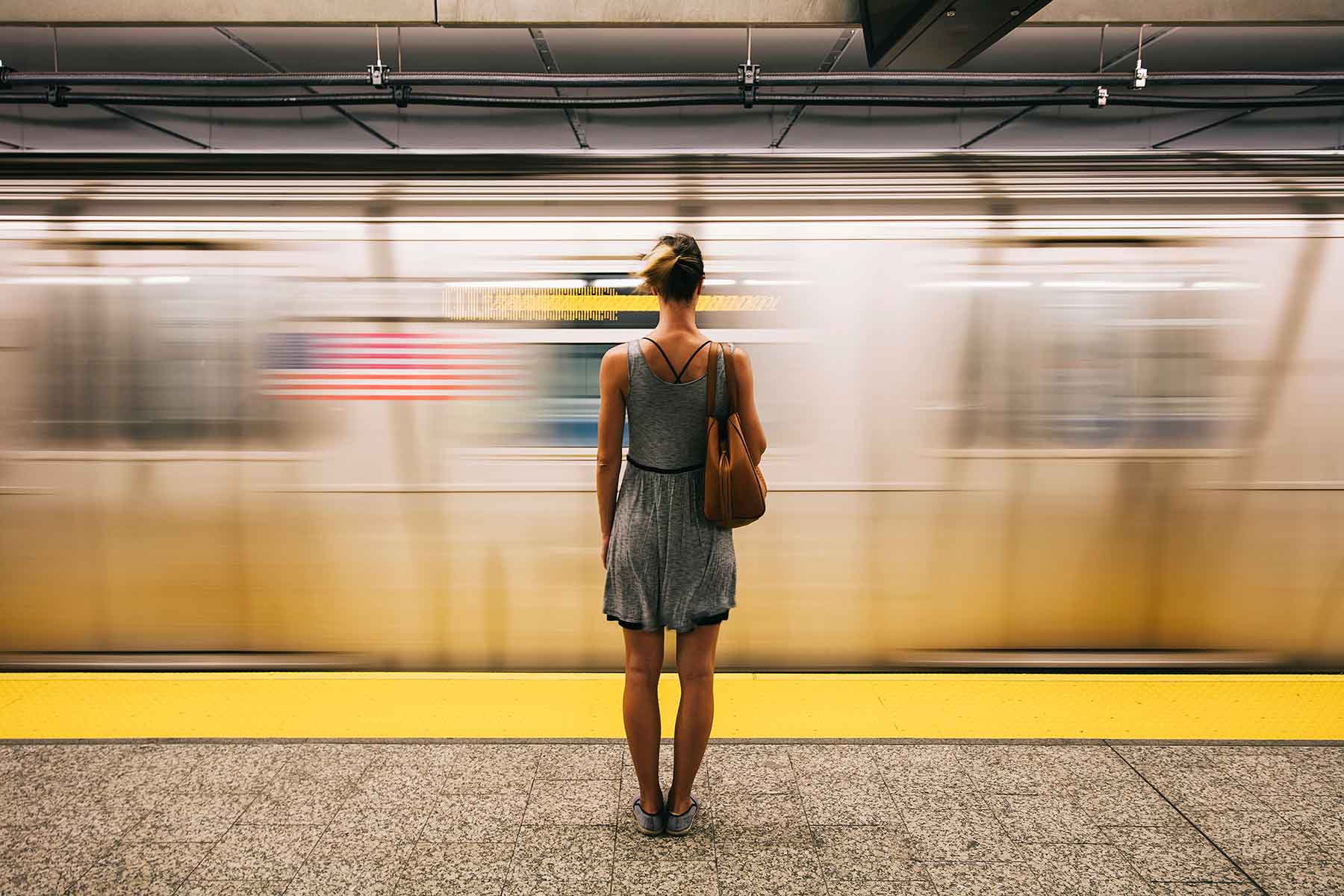 A woman standing on a train platform as the train speedily passes by