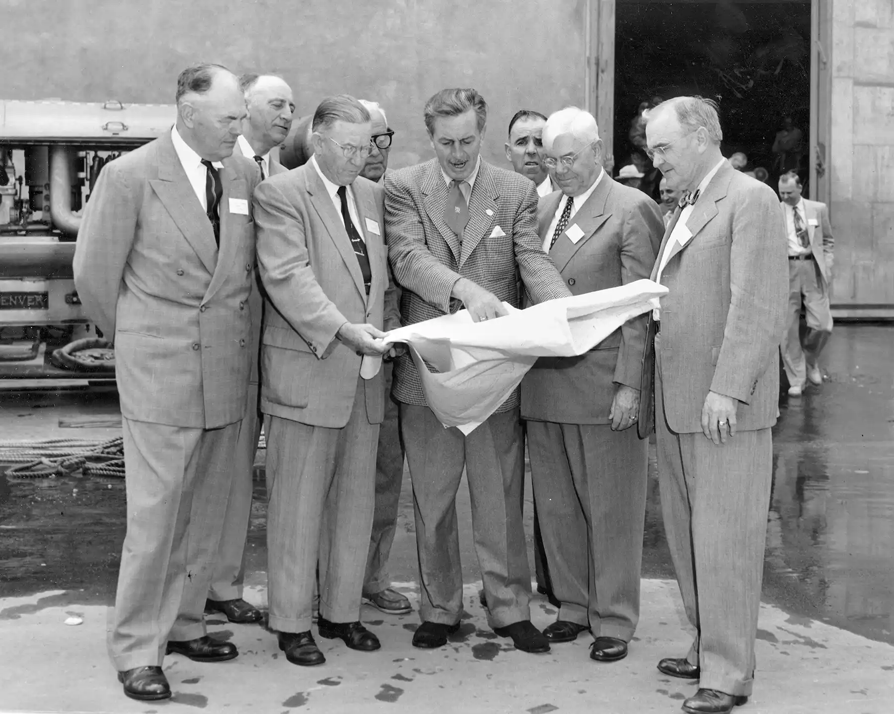 Walt Disney talking to a group of engineers about the blueprints of his theme park (we're assuming). 