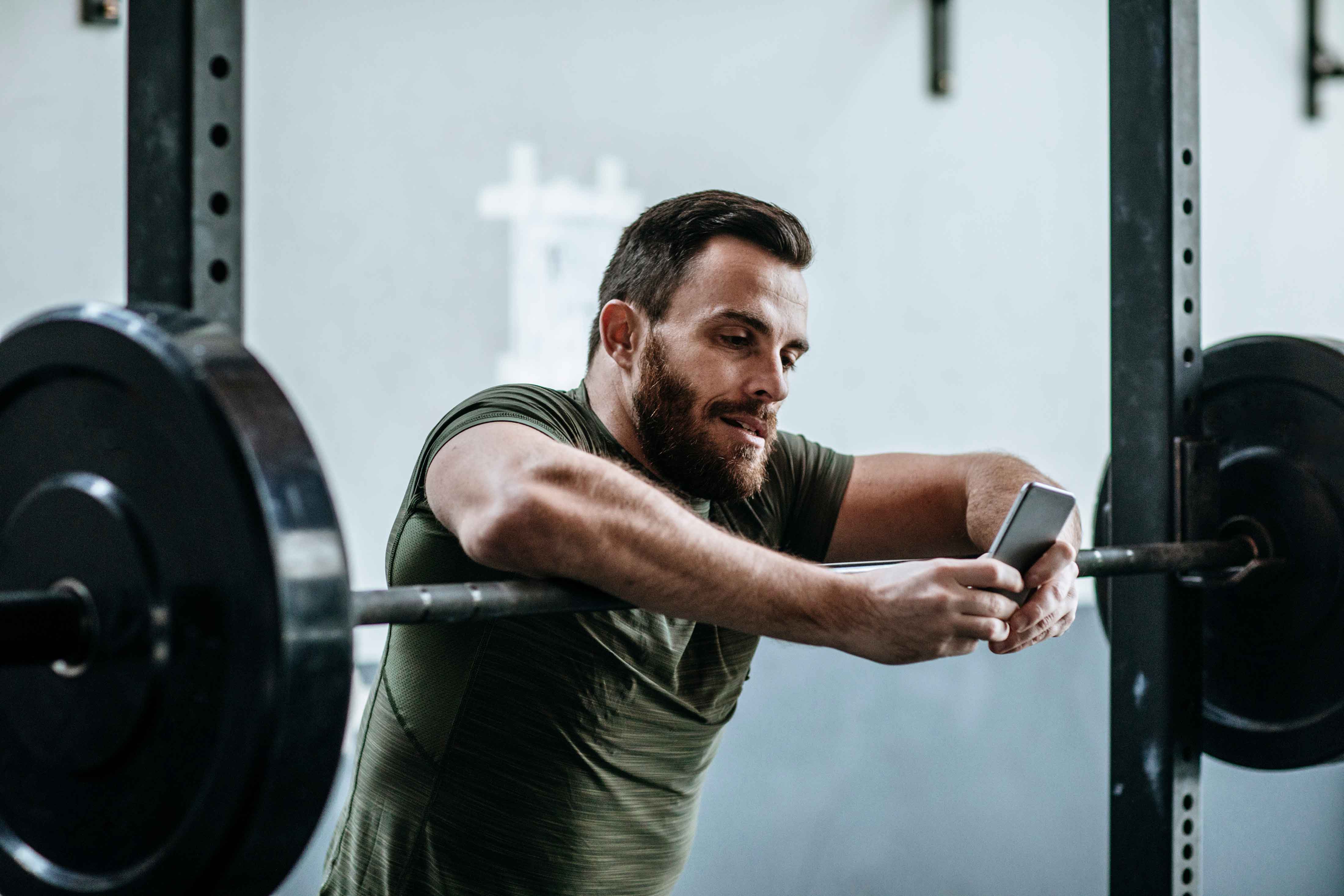 Man leaning over weight at gym, checking the status of his kids daycare on his phone.