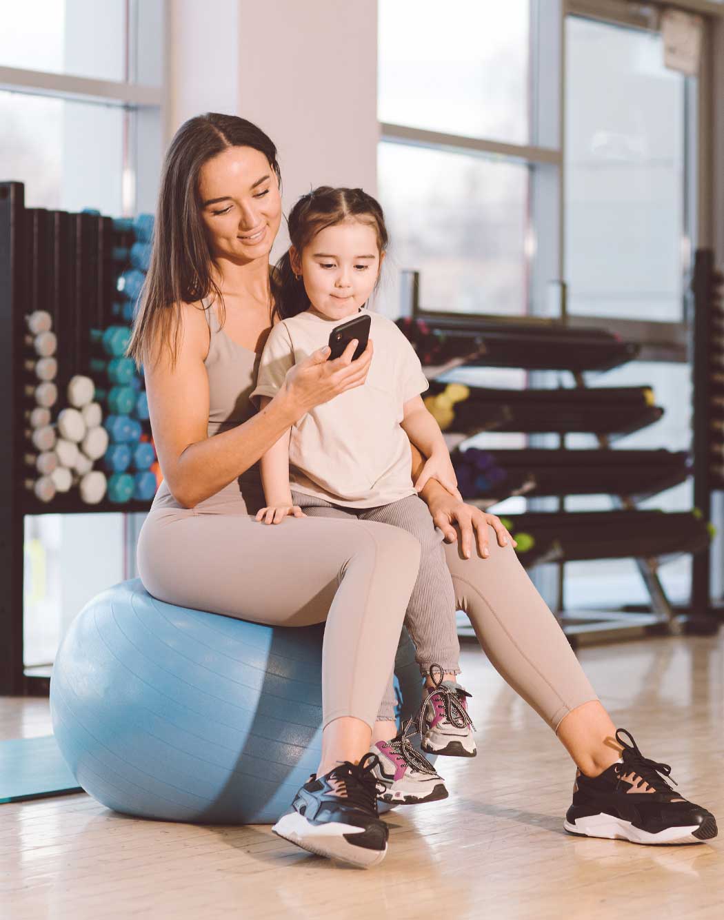 Woman with her daughter at the gym, checking her into childcare on her phone.