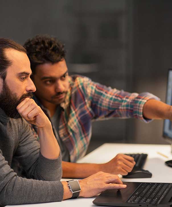 Two developers looking at a screen, while one of the developers points out an error in the code on the screen.