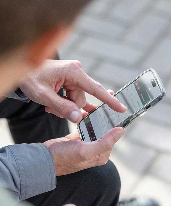 A hand holding a mobile phone and pointing to an app on the screen.