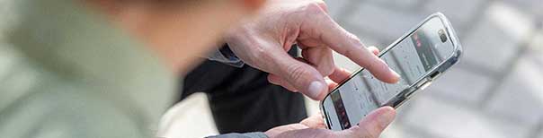 A hand holding a mobile phone and pointing to an app on the screen.