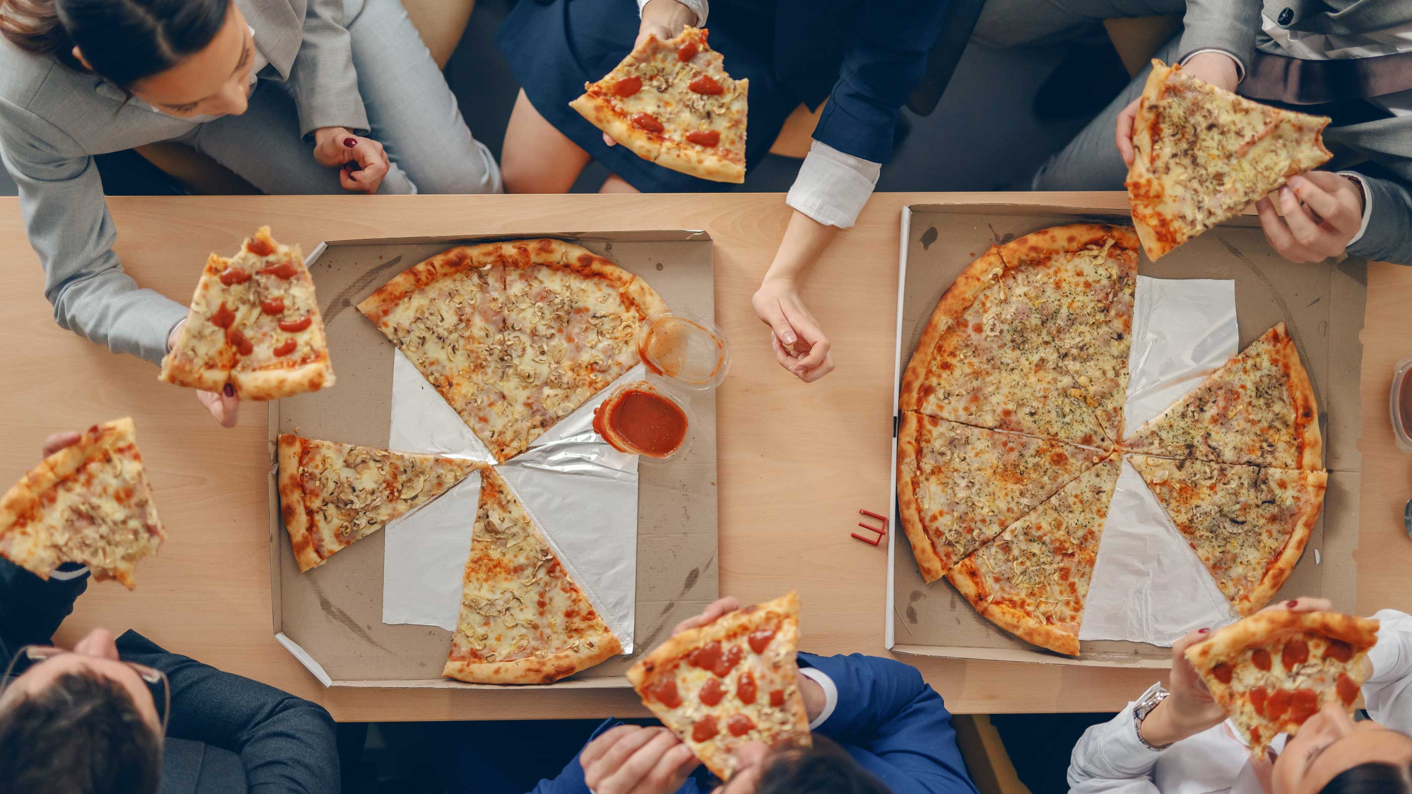 A small team enjoying 2 pizzas. 