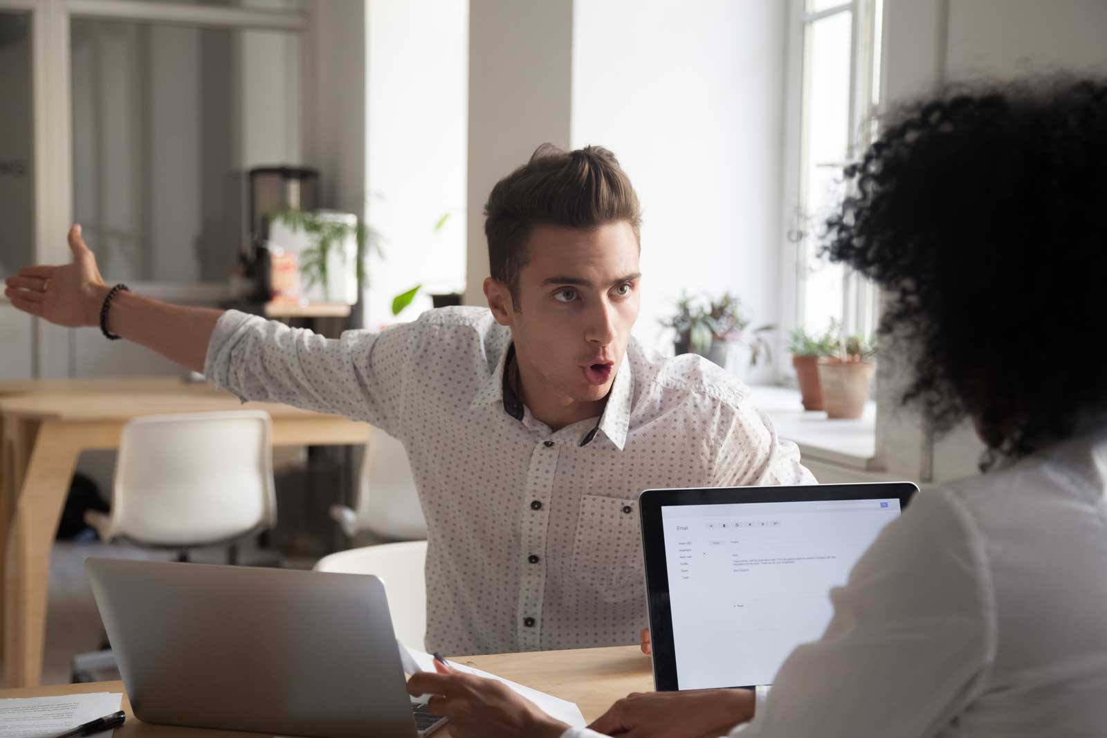 An angry man yelling at his coworker and gesturing towards the coworkers incompetence. 