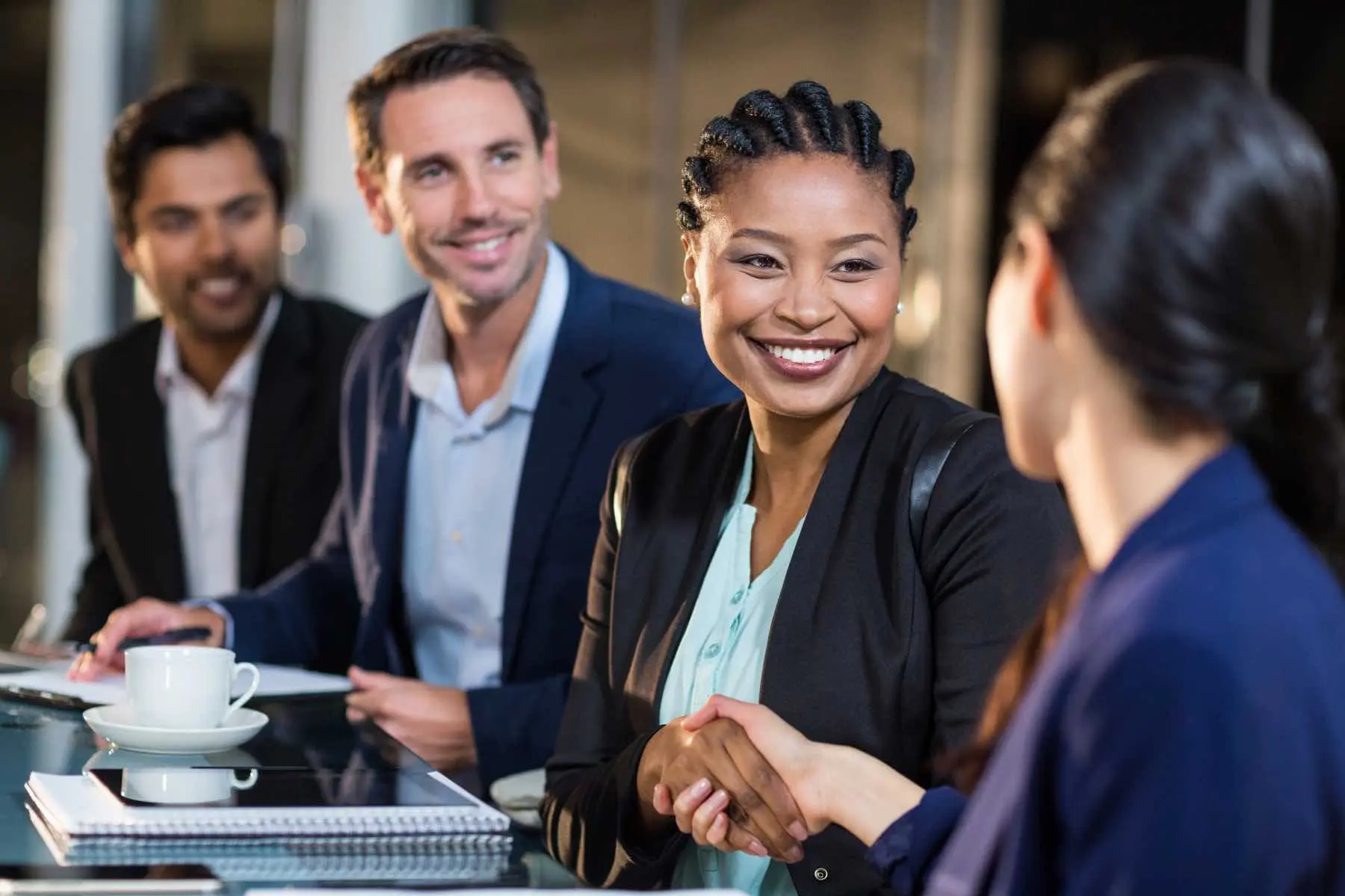 An executive shakes a candidate's hand while conducting an interview with two other executives present..