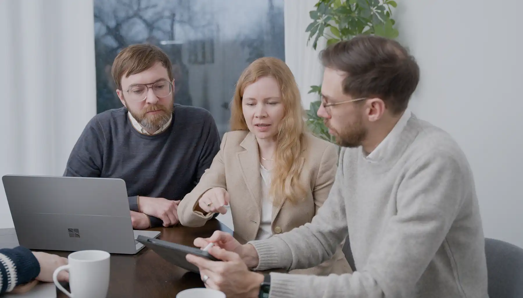 A lead UX developer shares his tablet with clients to discuss a possible new feature. One of the clients points at the screen to show they are questioning the new feature.