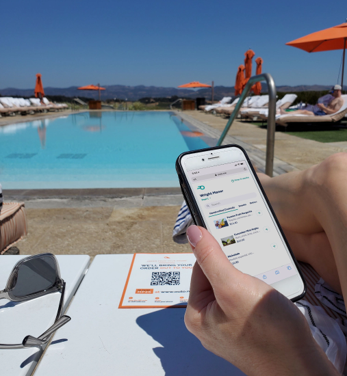 Woman lounging beside the resort pool, ordering her drink from her phone.
