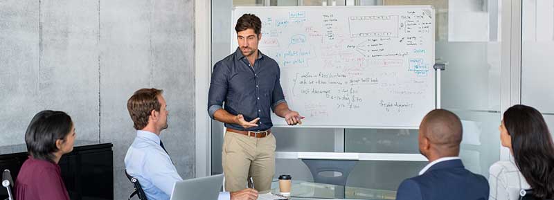 Several people in a meeting room with a man using a whiteboard. 