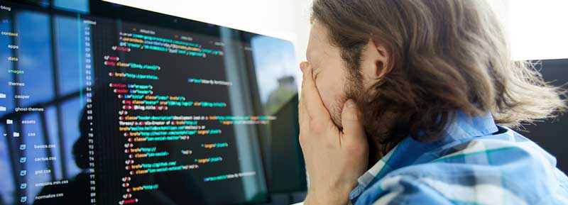 A frustrated developer burying his hands in his face in front of his computer screen of code.