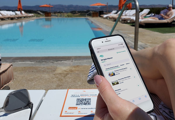 Woman lounges by pool at her resort with an app in her hand, ordering food and drink through the OUTOME app.